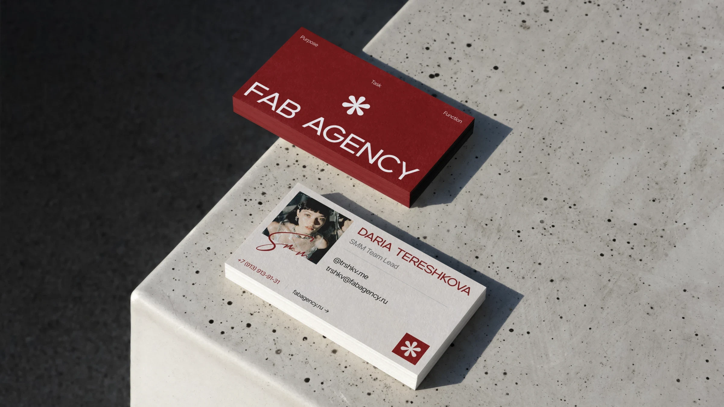 Визитки FAB.AGENCY на бетоне: красная с логотипом и белая с портретом сотрудника